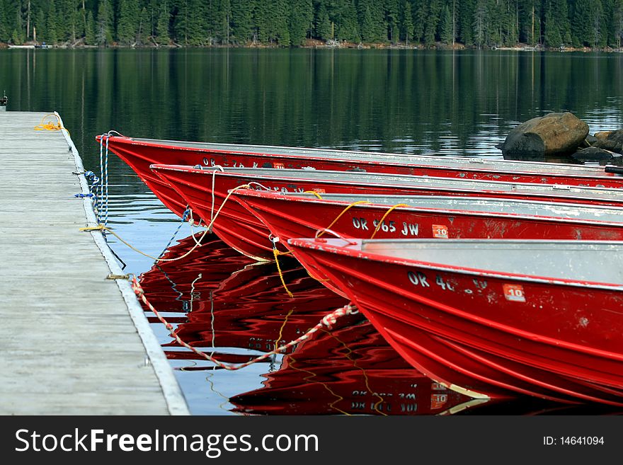 4 red boats tied up at a dock beside each other with pine forest and lake background. 4 red boats tied up at a dock beside each other with pine forest and lake background.
