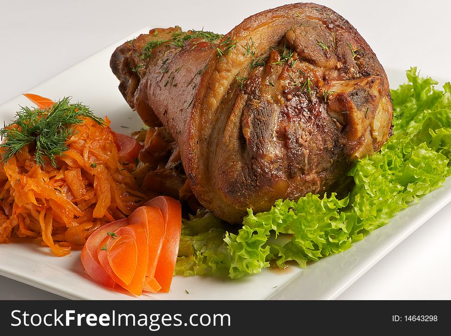 Roast pork leg rests on a plate with garnish, fresh tomatoes and lettuce. Roast pork leg rests on a plate with garnish, fresh tomatoes and lettuce