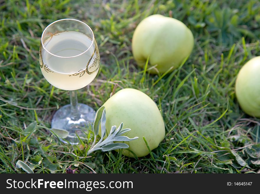 Glass of wine with green apples on the grass