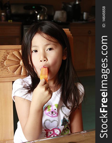 Little asia girl eating an orange ice pop. Little asia girl eating an orange ice pop