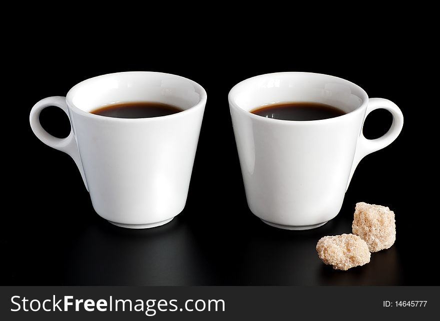 Two white cups of coffee and sugar cubes isolated on a black background. Two white cups of coffee and sugar cubes isolated on a black background