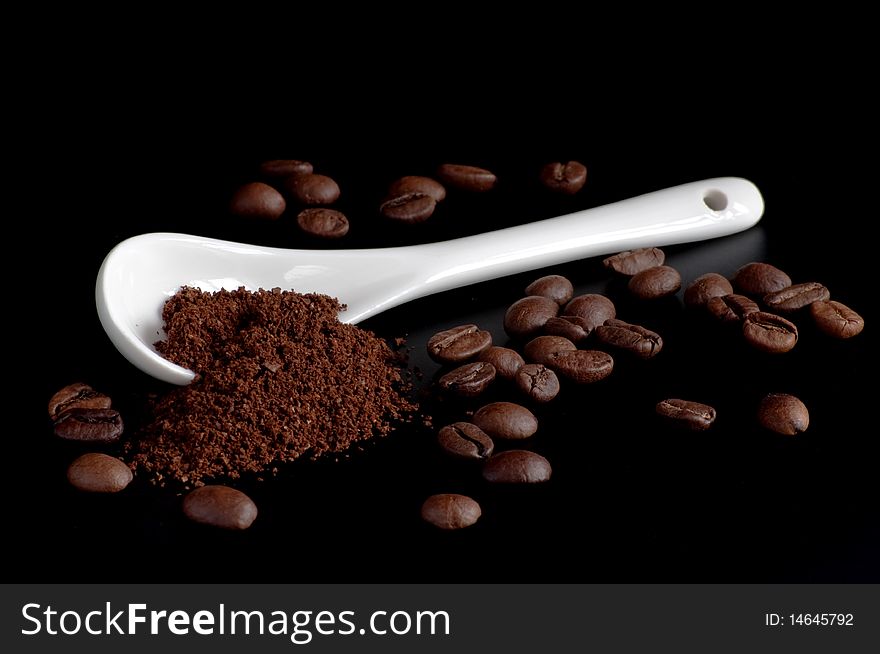 White spoon with coffee powder and beans on a black  background. White spoon with coffee powder and beans on a black  background