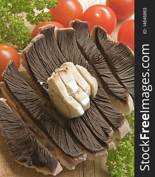 A closeup image of a large mushroom sliced together with cherry tomatoes and freshly picked parsley all on a wooden chopping board. A closeup image of a large mushroom sliced together with cherry tomatoes and freshly picked parsley all on a wooden chopping board.