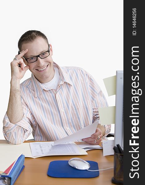 A man is seated at a computer desk and smiling at the camera.  Vertical shot.  Isolated on white. A man is seated at a computer desk and smiling at the camera.  Vertical shot.  Isolated on white.