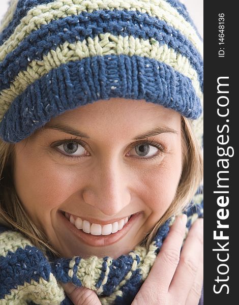 An attractive young woman is smiling and wearing a blue and beige knit cap and scarf. Vertical shot. An attractive young woman is smiling and wearing a blue and beige knit cap and scarf. Vertical shot.