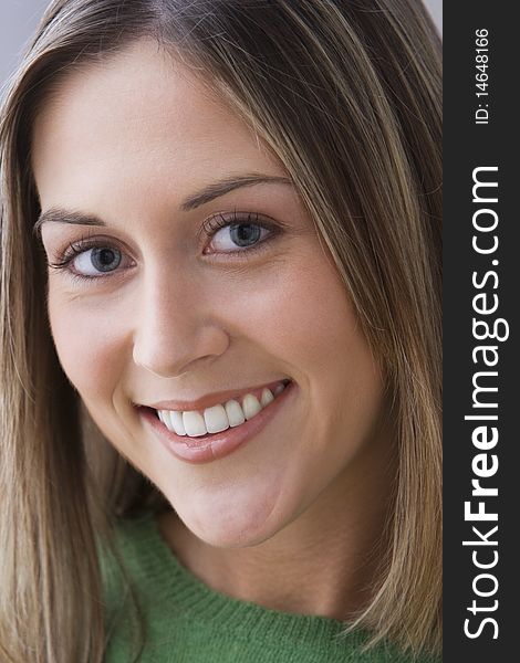 An attractive young woman is wearing a green sweater and smiling at the camera. Vertical shot. An attractive young woman is wearing a green sweater and smiling at the camera. Vertical shot.