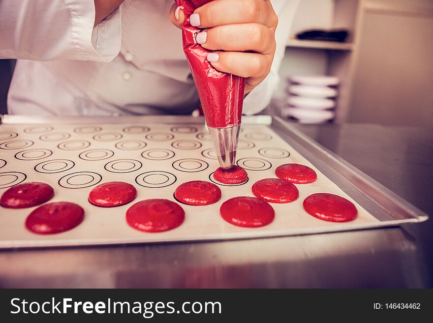 Conscious work. Professional confectioner using piping bag while putting dough on baking tray. Conscious work. Professional confectioner using piping bag while putting dough on baking tray