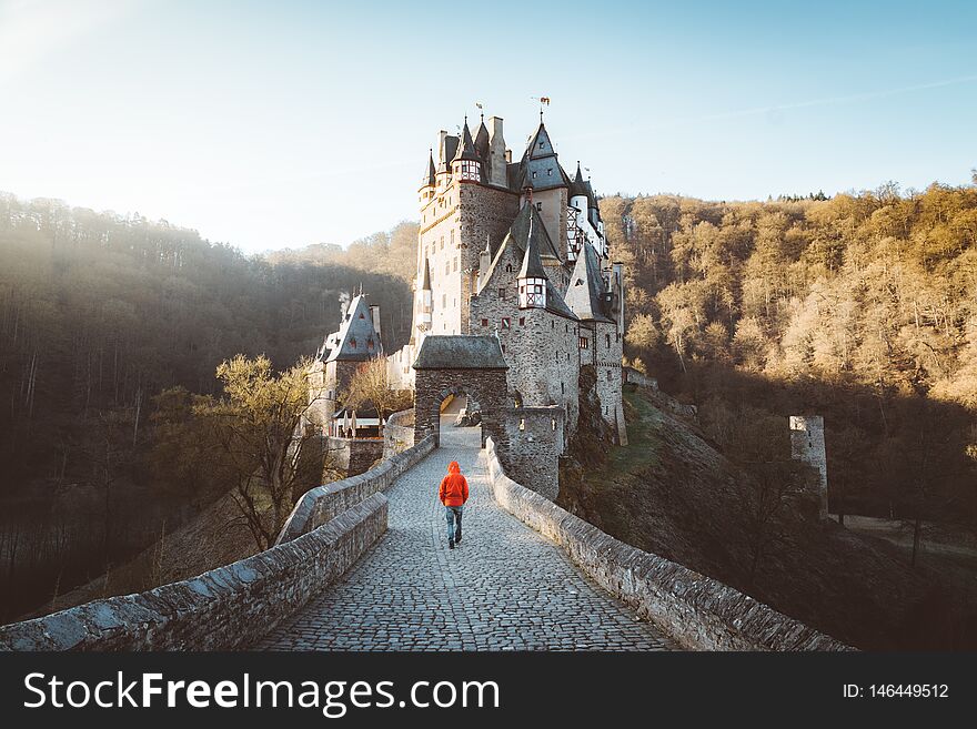 Panorama view of young explorer with backpack taking in the view at famous Eltz Castle at sunrise in fall, Rheinland-Pfalz, Germany. Panorama view of young explorer with backpack taking in the view at famous Eltz Castle at sunrise in fall, Rheinland-Pfalz, Germany