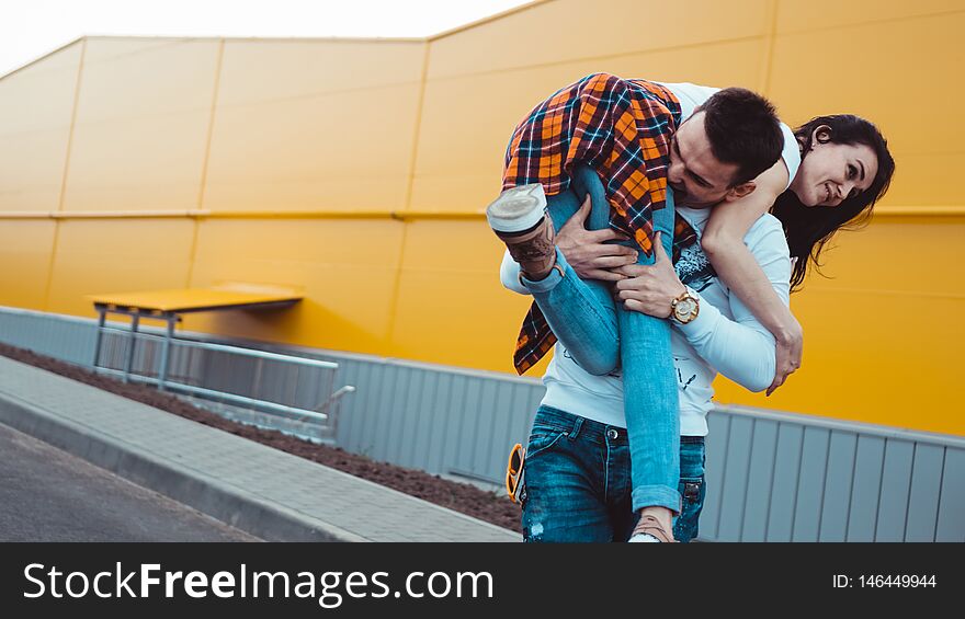 Happy men carrying his girlfriend on yellow background - couple in love. Happy men carrying his girlfriend on yellow background - couple in love