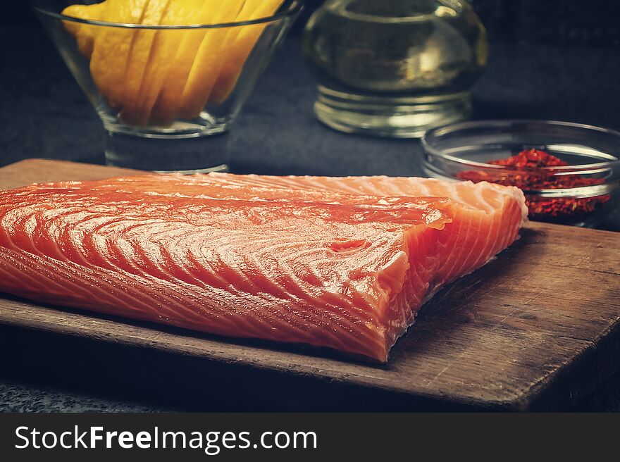 Piece of salmon fillet on a wooden cutting board with ingredients for its further preparation - photo, image