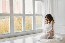 Beautiful Young Pregnant Woman With Fashionable Hairstyle In A Stylish Peignoir Smiling And Posing Near The Big Window Royalty Free Stock Images