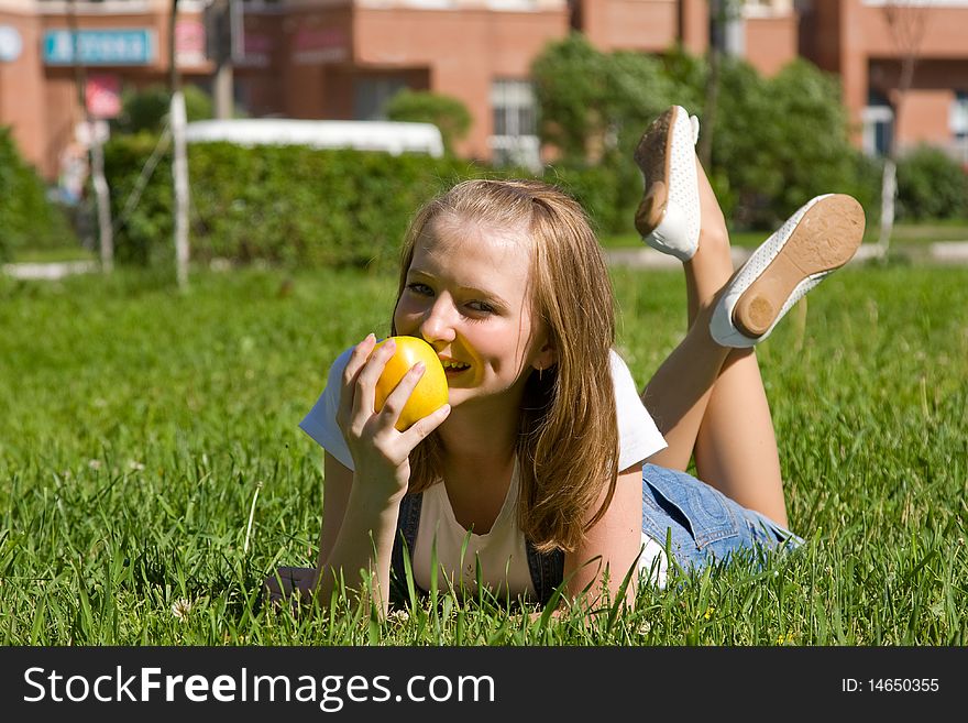 Teenage girl with a yellow apple. Beautiful young woman lying on a green grass and eating apple outside on field.