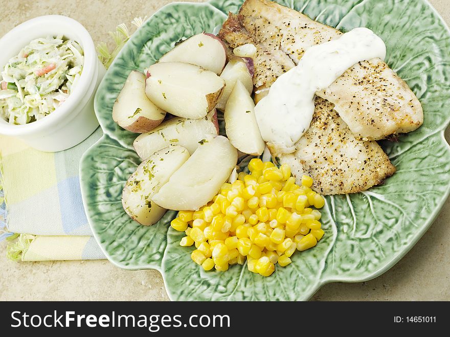 A broiled tilapia dinner with potatoes, corn and coleslaw. A broiled tilapia dinner with potatoes, corn and coleslaw