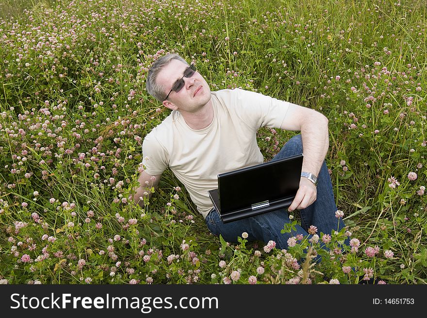 Thoughtful man with laptop on meadow