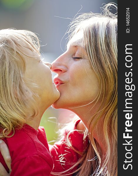 Mother kissing her son with long blond hair outdoors. Mother kissing her son with long blond hair outdoors