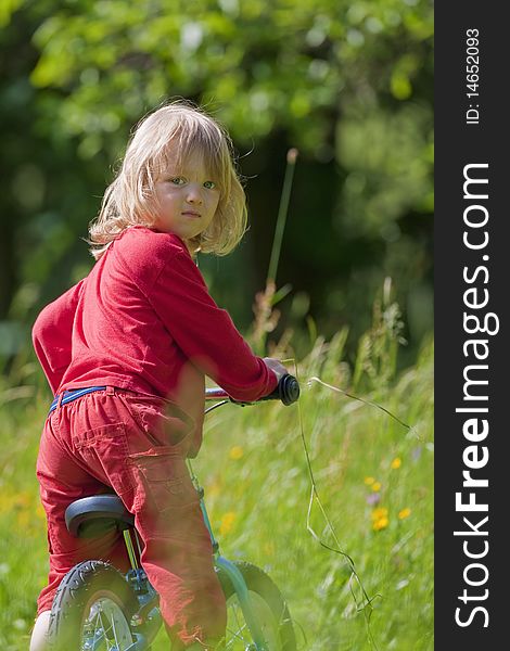 Boy with long blond hair riding a bike in the garden. Boy with long blond hair riding a bike in the garden