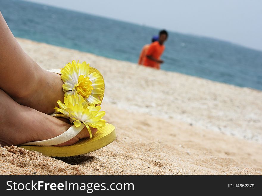 Yellow flowered sandals relax on a sandy beach, with the ocean in the background.  It's sunny, hot and relaxing. Yellow flowered sandals relax on a sandy beach, with the ocean in the background.  It's sunny, hot and relaxing.