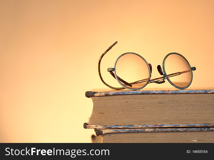 Old spectacles lying on ancient books isolated on yellow background