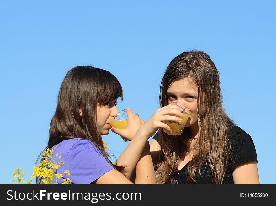 Two beauty teenage girls drinking orange juice against the blue sky