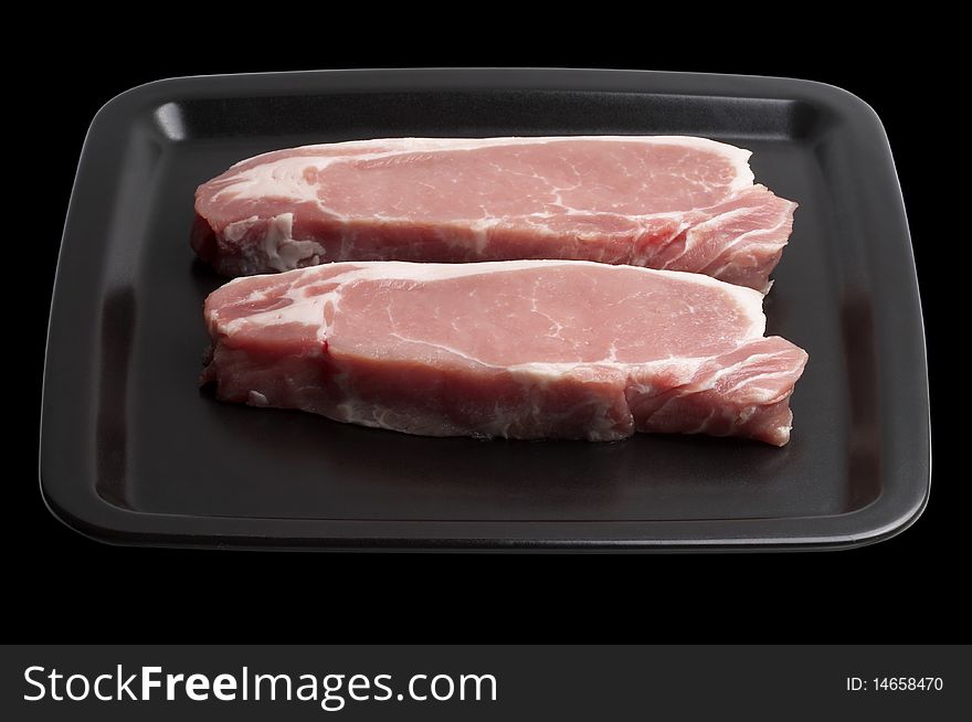 Two raw pork steaks on the dark square plate isolated over black background