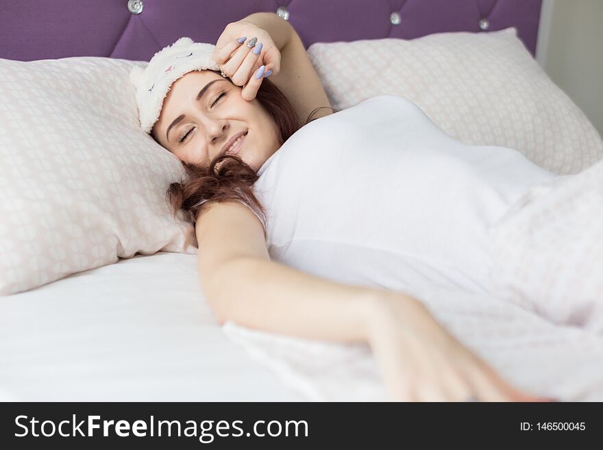 An attractive young brunette girl woman wakes up in her bed in a sleep mask.