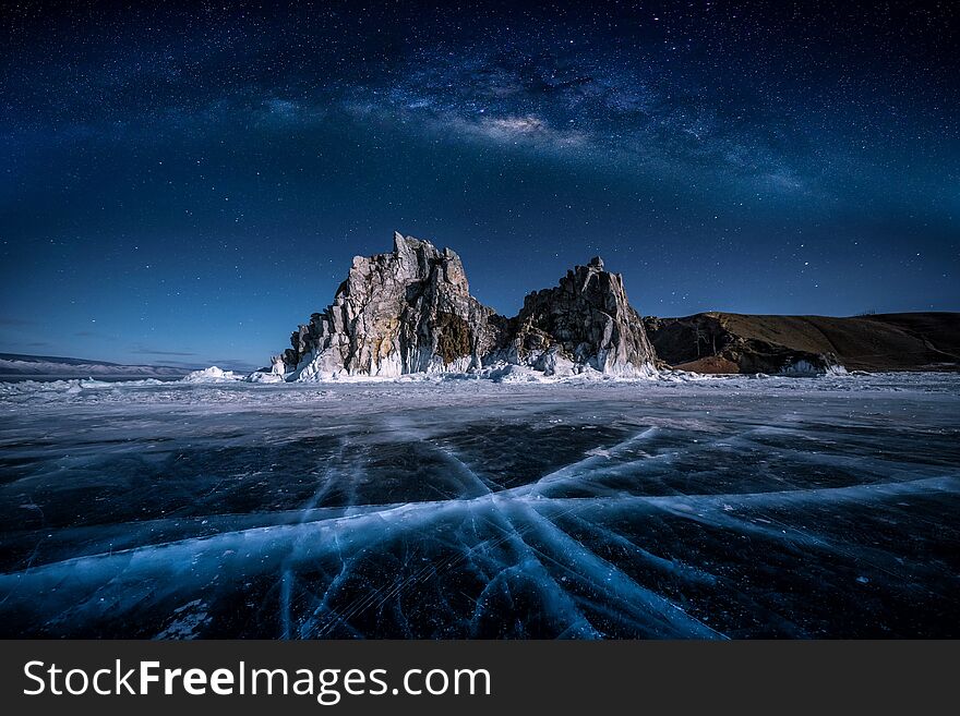 Landscape of Shamanka rock and milky way on sky with natural breaking ice in frozen water on Lake Baikal, Siberia, Russia