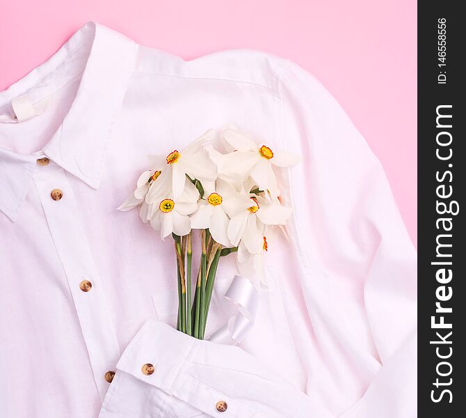 Delicate spring bouquet of white daffodils on a white basic shirt on a pink background. Top view, flat lay. Delicate spring bouquet of white daffodils on a white basic shirt on a pink background. Top view, flat lay