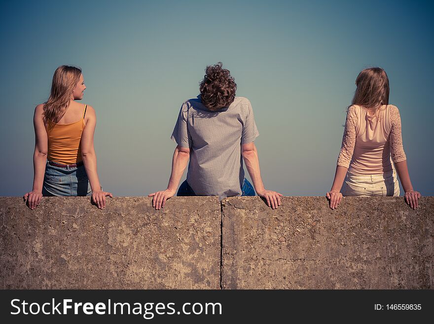 Happiness summer friendship concept. Group of friends spending time together having fun outdoor sitting on wall against blue sky