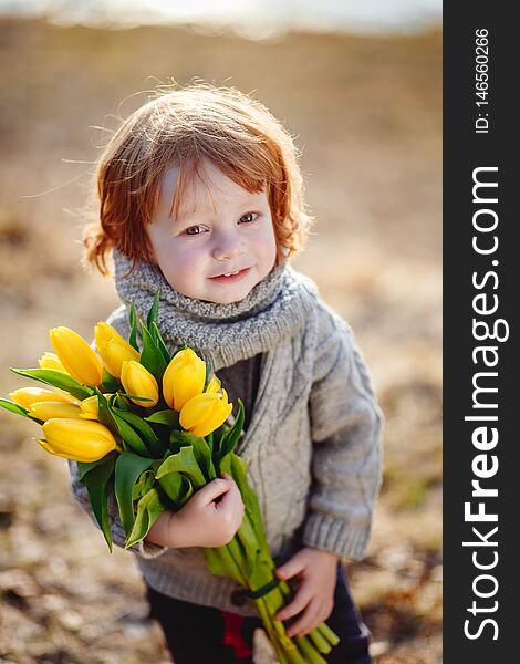 A Cheerful Cute Little Boy With Red Hair Holding Yellow Tulips Outside In Early Spring In The Forest Near The Water.