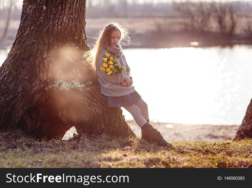 A girl with yellow tulips in early spring on a cold evening near the river