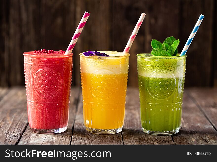 Three smoothies with fine detail decoration on top of them, various fruit smoothies