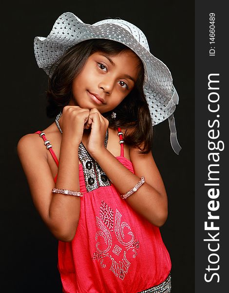An Indian girl child posing with a smile wearing a white hat and red dress. Black background. An Indian girl child posing with a smile wearing a white hat and red dress. Black background