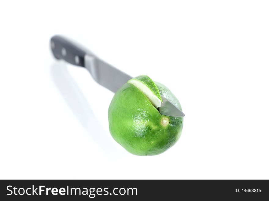 A lime being cut by a chefs knife with shadow in isolation with one section showing. A lime being cut by a chefs knife with shadow in isolation with one section showing