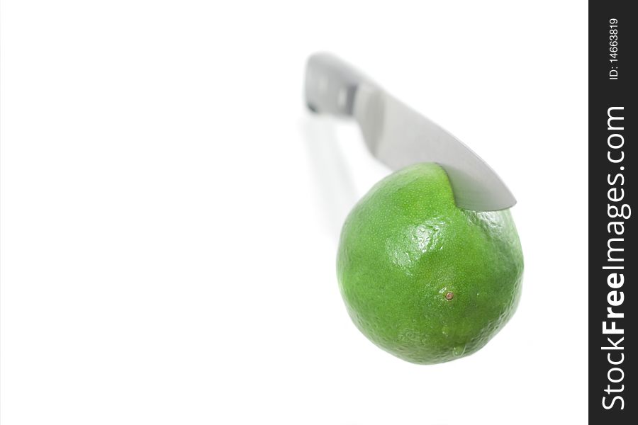 A lime being cut by a chefs knife with shadow in isolation. A lime being cut by a chefs knife with shadow in isolation