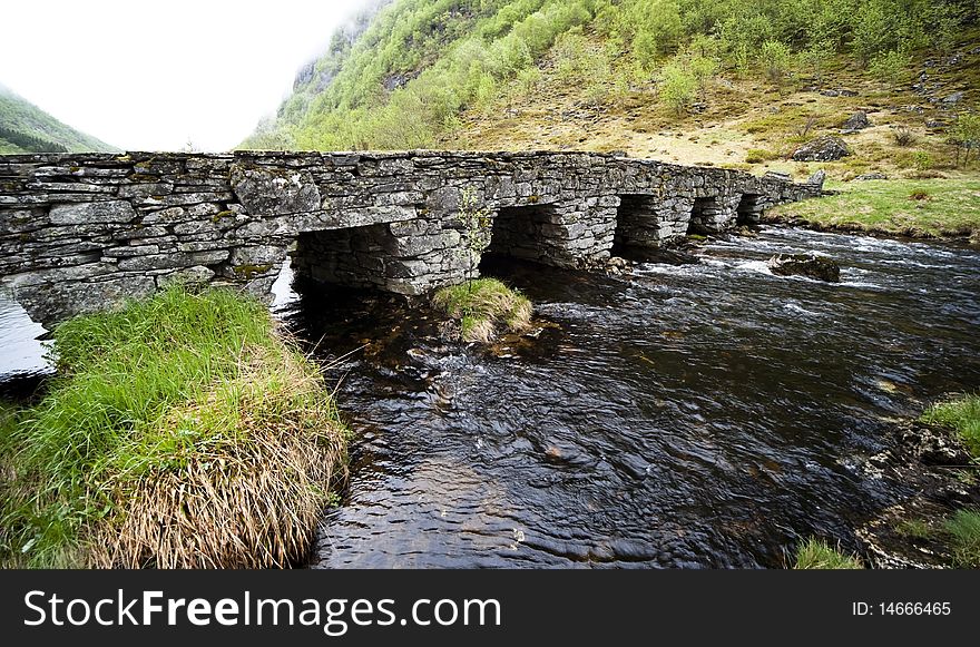 A very old stone bridge across a small river in Norway. A very old stone bridge across a small river in Norway