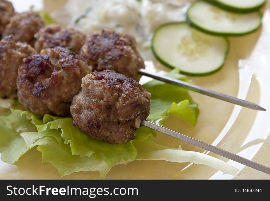 Meat balls on a metal stick with cucumber a tzatziki salad in the back. Meat balls on a metal stick with cucumber a tzatziki salad in the back.