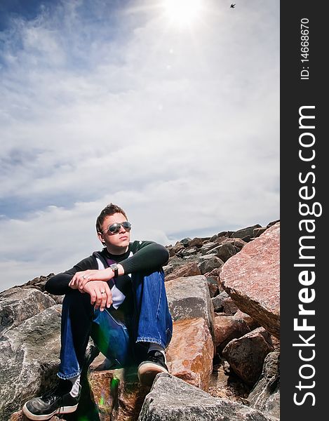 Young man on the rocks on clouds background in the eyeglasses