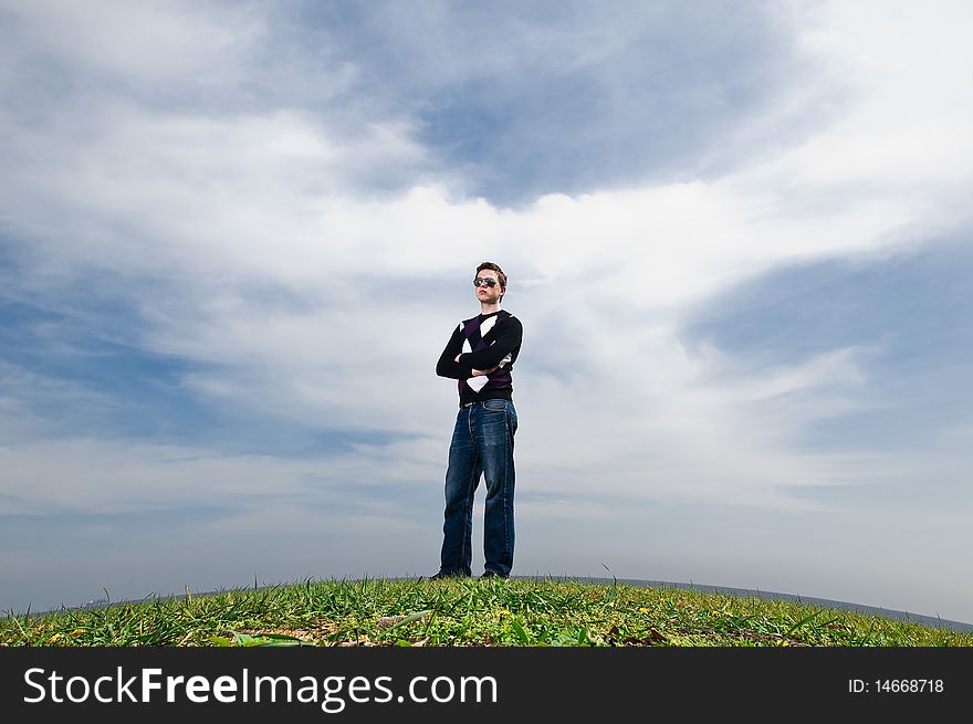 Young man in the clouds on the green grass in the eyeglasses