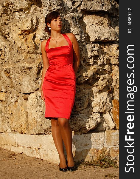 The beautiful girl in a red dress poses at a rock