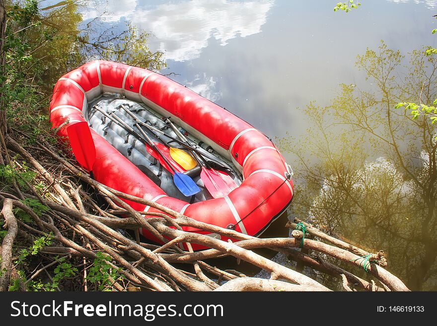 Red inflatable boat with oars raft for rafting along a  river against the sky reflected in the water. View from above