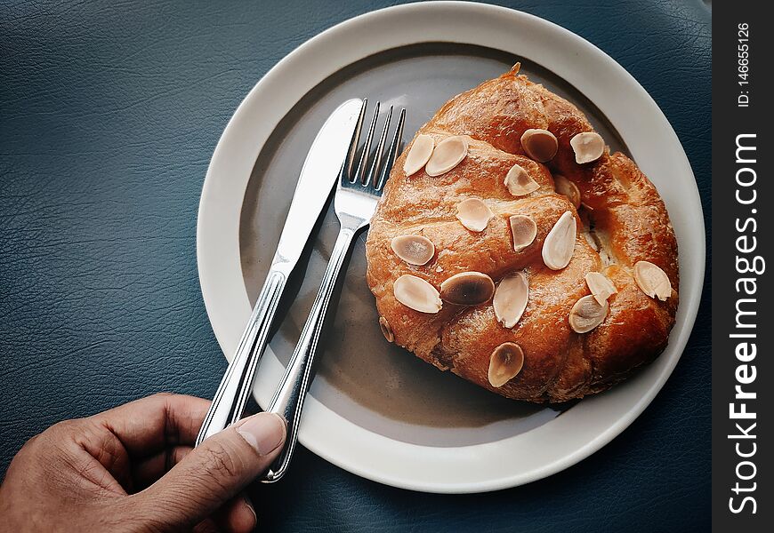 Hand Is Picking Knife And Fork To Eat The Croissant With Sliced Almonds On The Top.