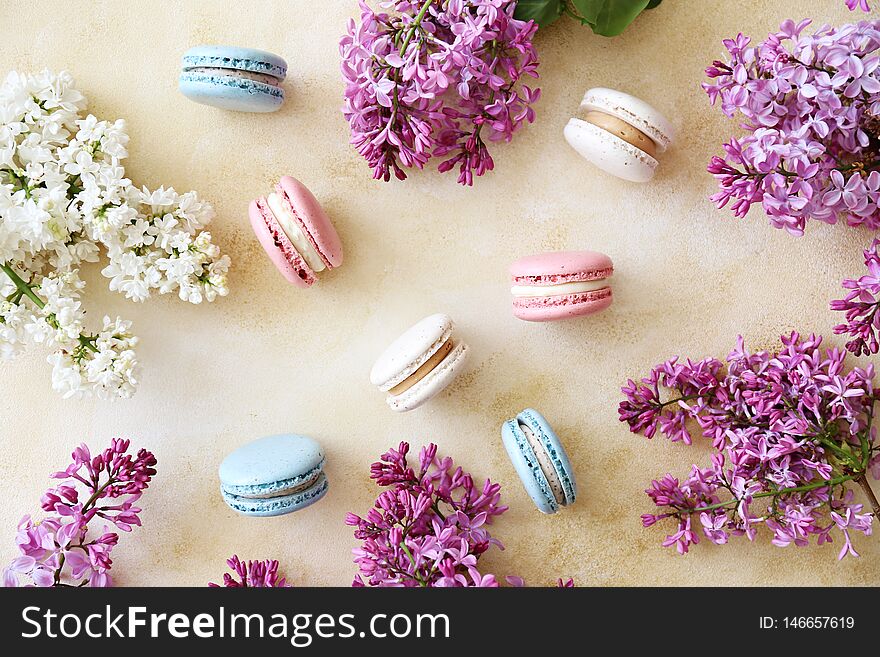 Minimalistic composition with bunch of french macaron sweets of different color and taste, lilac flowerings scattered over yellow concrete texture background. Top view, close up, flat lay, copy space. Minimalistic composition with bunch of french macaron sweets of different color and taste, lilac flowerings scattered over yellow concrete texture background. Top view, close up, flat lay, copy space