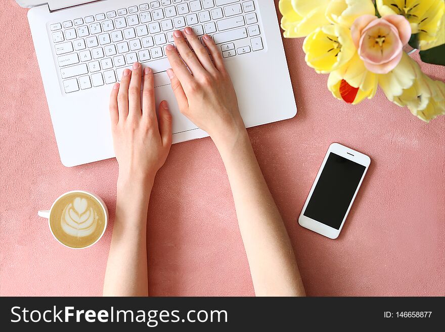 Top view shot of woman typing on white laptop computer, concrete textured table background. Feminine workspace with flowers bouquet. Close up, copy space. Top view shot of woman typing on white laptop computer, concrete textured table background. Feminine workspace with flowers bouquet. Close up, copy space