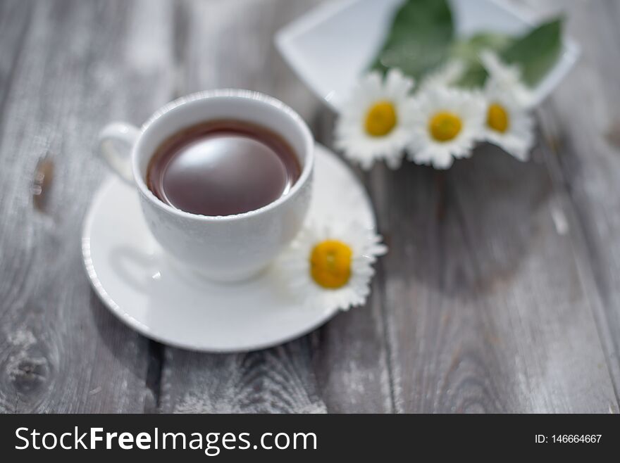 Tea in a white cup on a wooden table. Daisies on the table