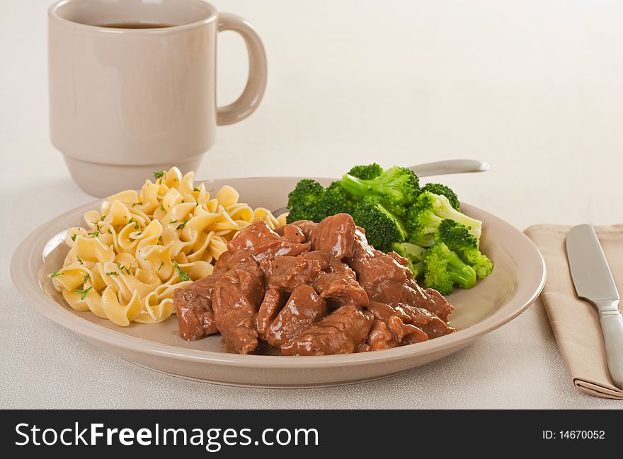 Beef tips topped with gravy with egg noodles, broccoli and a drink. Beef tips topped with gravy with egg noodles, broccoli and a drink