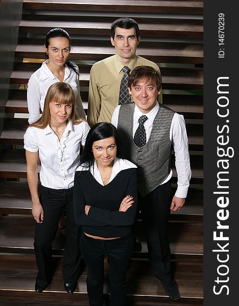 A group of five young business people in formal clothes is standing on the stairs. A group of five young business people in formal clothes is standing on the stairs.