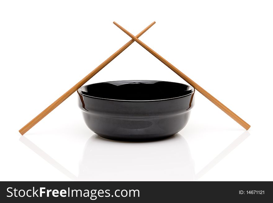 Crossed chopsticks on a black bowl on white