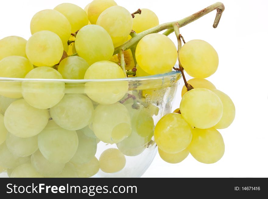 Close and low level angle capturing a glass bowl of grapes arranged over white. Close and low level angle capturing a glass bowl of grapes arranged over white.