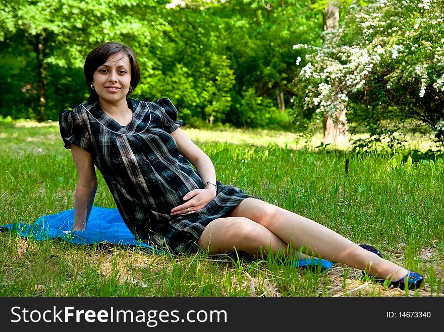 Beautiful smiling pregnant woman relaxing on grass in park.