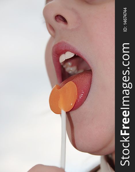 Girl licking an orange lollipop